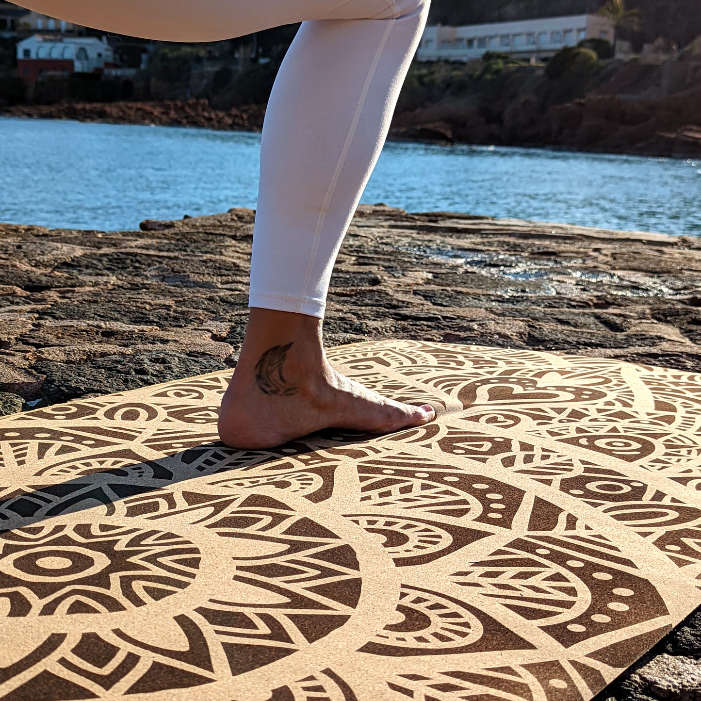 Close-up of the MandaLove ZenMotion cork yoga mat with the foot of a yogini placed on it, against the backdrop of a serene sea.